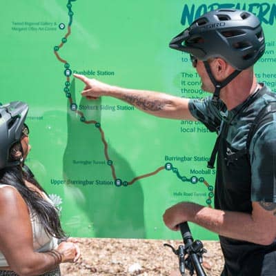 man in bike helmet pointing at rail trail map