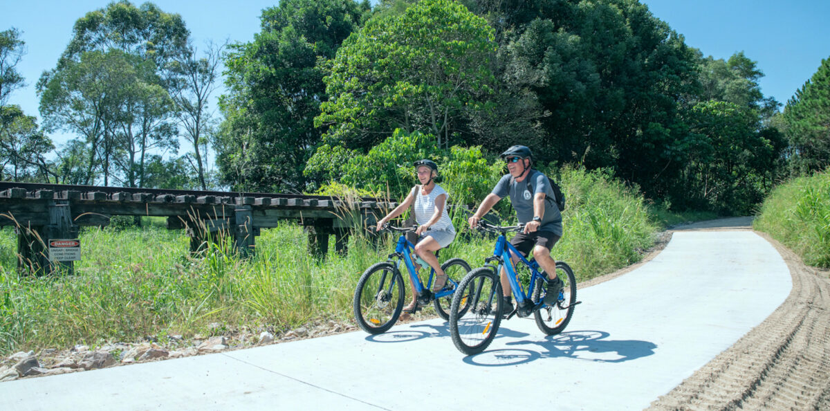 a man and woman riding e-bikes on a rail trail
