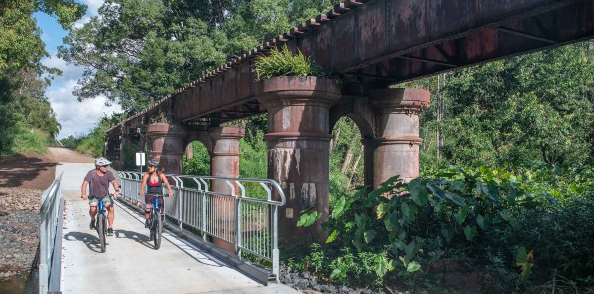 couple riding an ebike next to a rail bridge